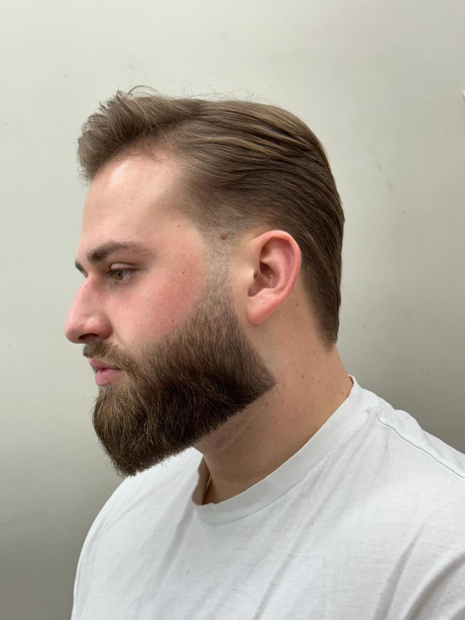 Cliente de perfil com barba longa desenhada e cabelo penteado para trás