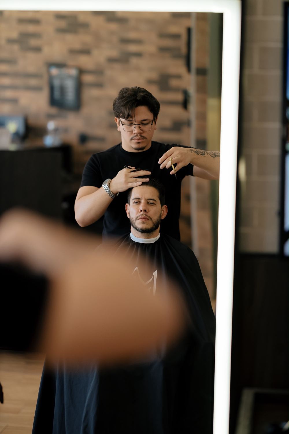 Barbeiro finalizando corte de cliente refletido no espelho iluminado